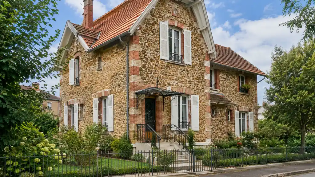 Maison meulière ancienne avec façade en pierre rugueuse, encadrements en brique et volets blancs